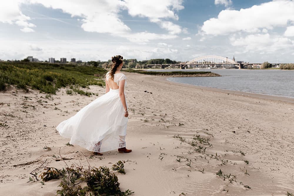 Bruid in bohemian trouwjurk met laarsen aan op het strand.